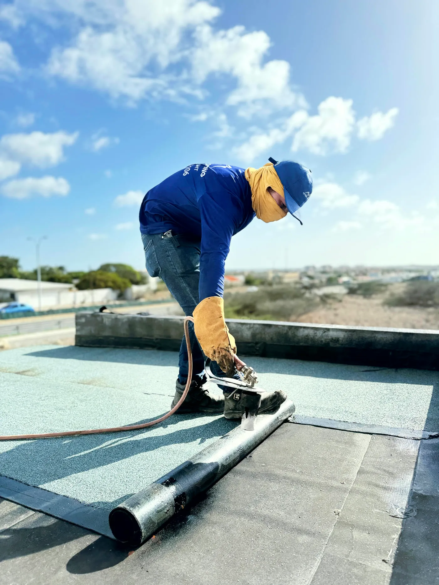 Optimo crew member rolling out membrane with a seam roller on a flat roof in Aruba